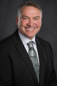 A photo of Kelowna Mayor Tom Dyas wearing a black suit jacket with a white shirt and grey patterned tie.